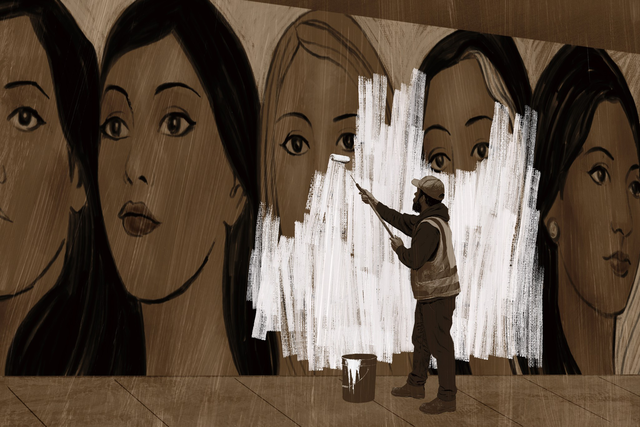 A person is painting over a mural of five women’s faces with white paint using a roller.